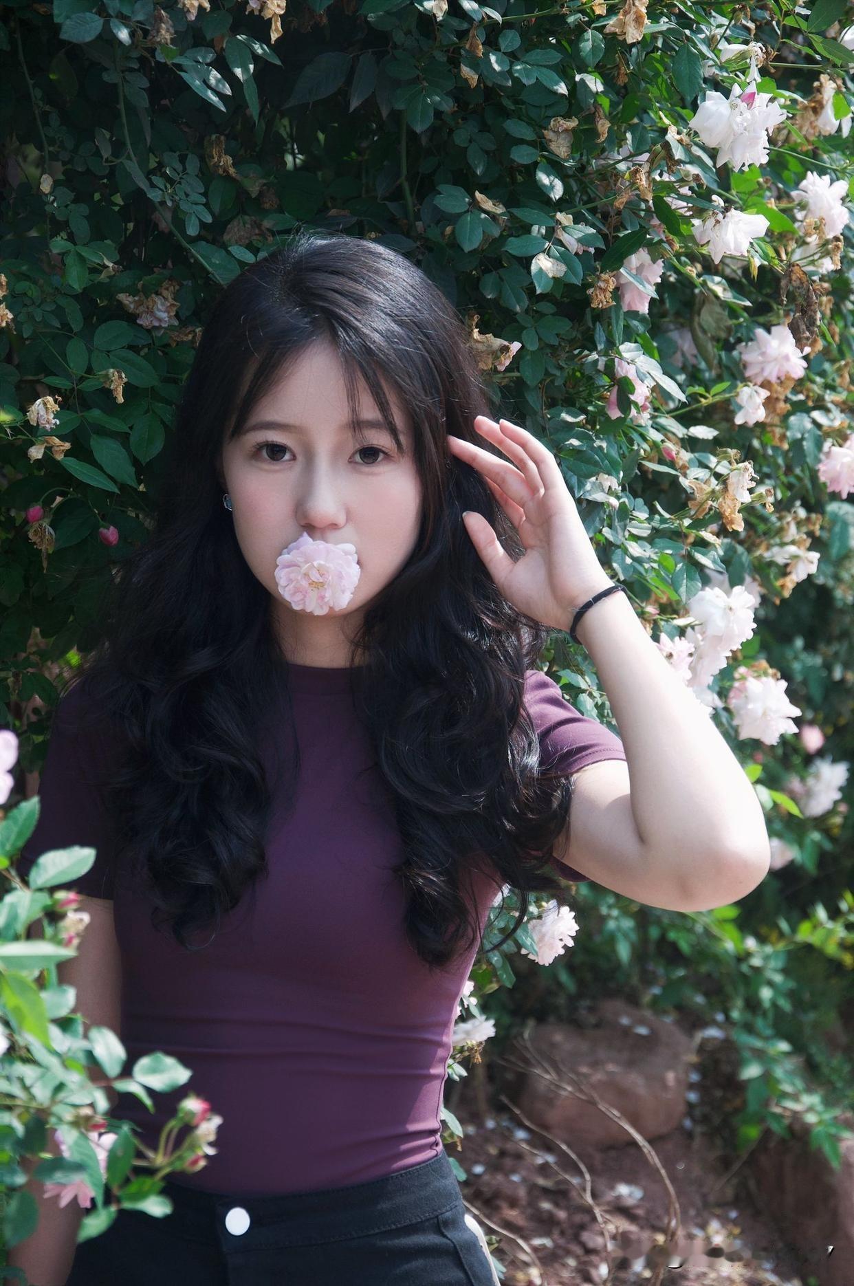 她站在花丛中，嘴巴含着一朵花，那画面就像从画里走出来的一样。这让我想到拍油菜花时