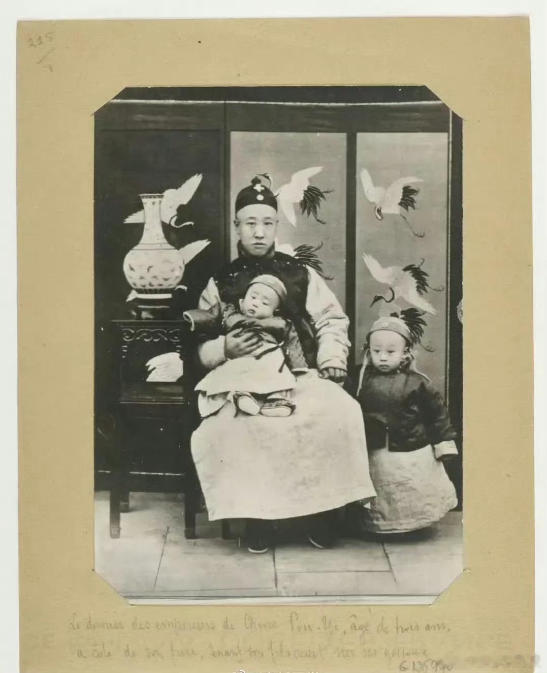1909年，北京。晚清，刚满三岁的溥仪。他站在父亲身边，父亲载沣坐在大圈椅上，膝