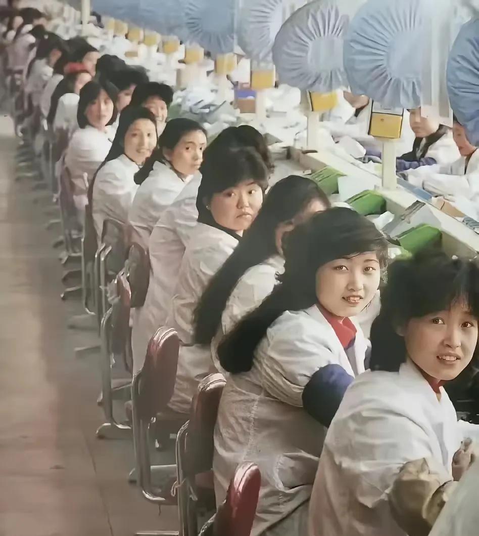 这是1986年三峡电器厂电风扇生产车间，一排女工坐在生产工位，呆呆的望向镜头，眼