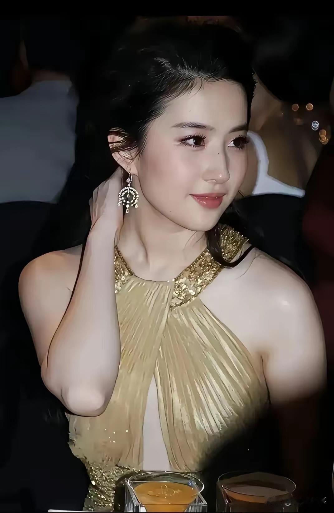 香槟礼裙之下，惊艳全场的女明星。镜头下的她，她身着一件挂脖礼服，精致的金色颈饰顺