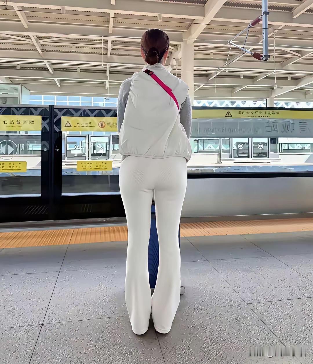 这姑娘坐在地上，穿着亮黄色外套和白色裤子，旁边放着一个粉色小包。