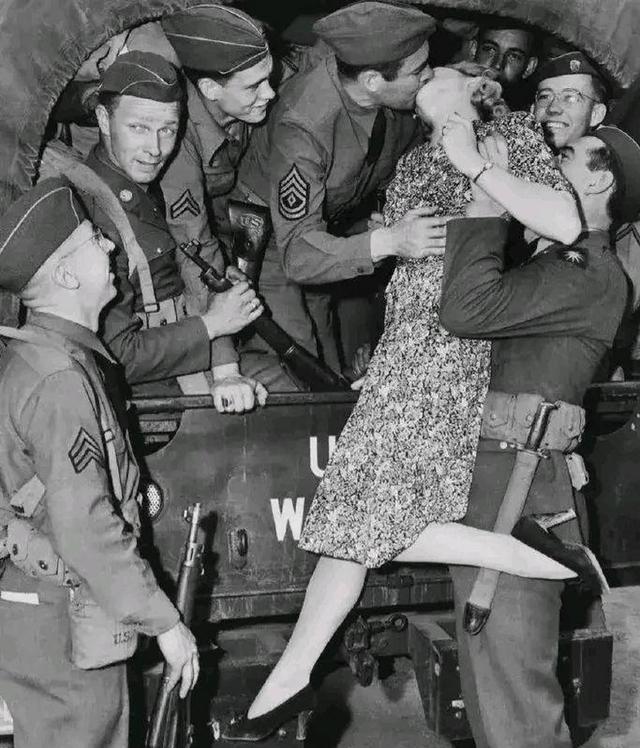 1940年，一名士兵举起一名年轻貌美的女人，将她送给卡车上的大兵，大兵见到女子不