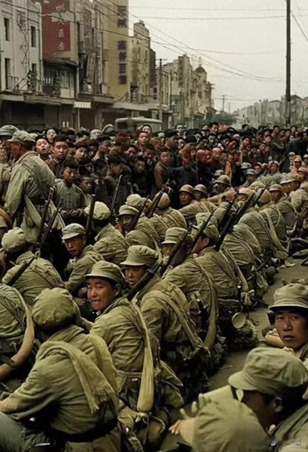 1949年，南京街头，席地而坐的解放军战士。镜头下的他们身穿统一军装、手扛钢枪的