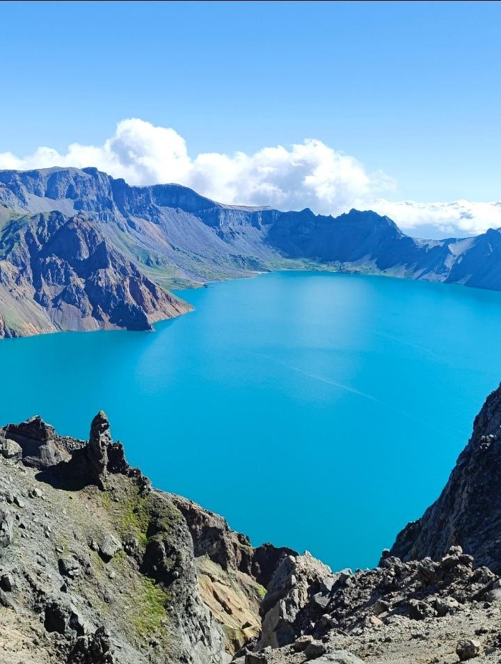 这抹澄澈的蓝，是长白山天池给人间的惊喜。火山岩壁环伺着一汪宝石色的湖水，云絮缠在