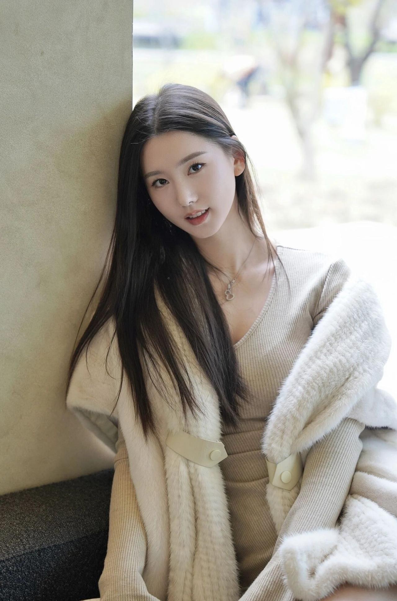 冬日暖阳下，温柔少女倚靠墙边，毛绒外套温暖相伴。