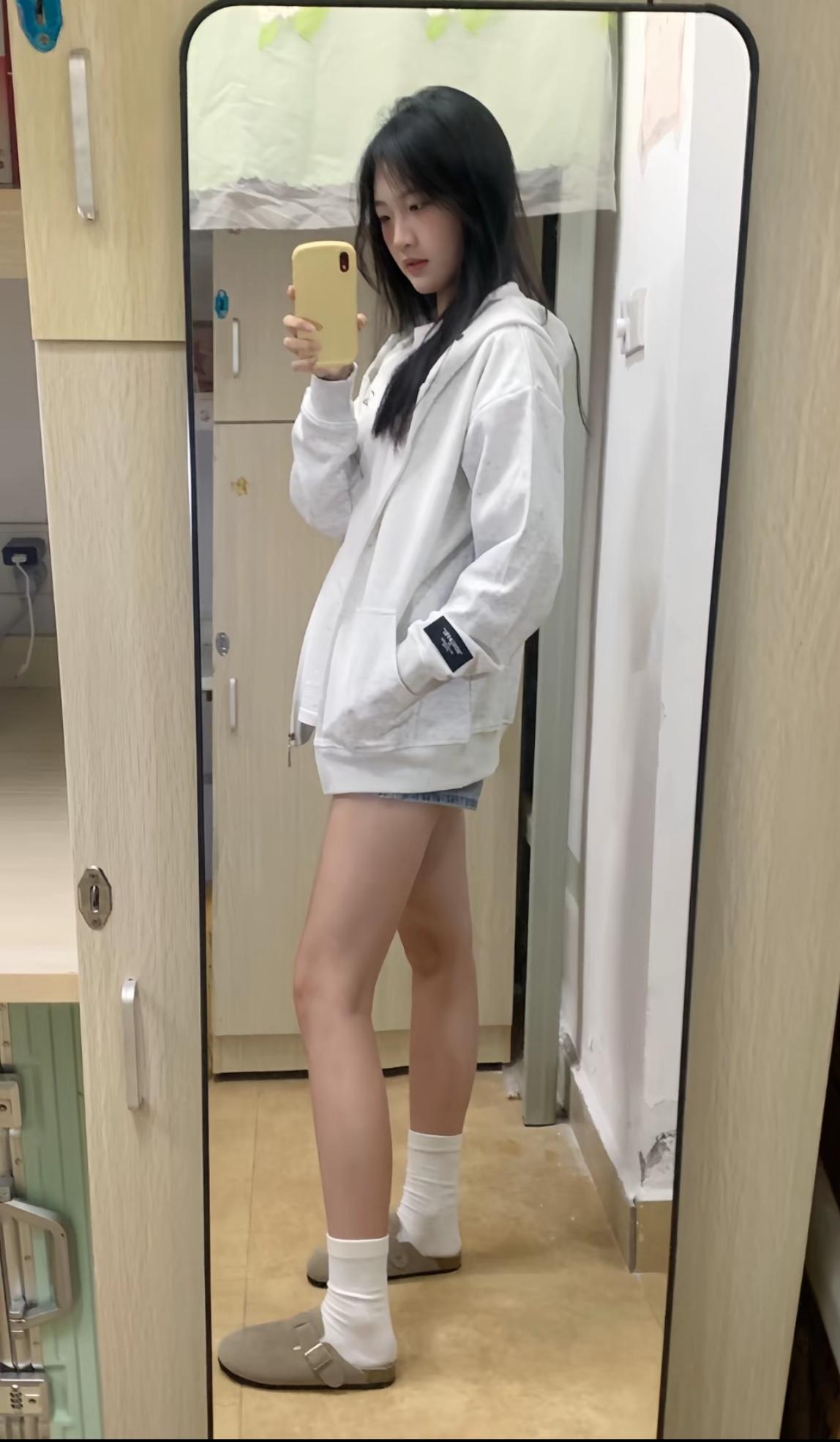 小女孩对着橱镜拍镜子里的自己。