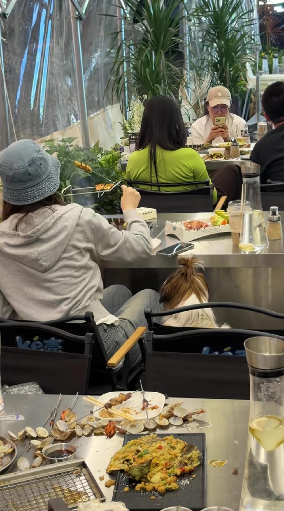 山东某地一烧烤店铺，网友拍摄到的女子让自己的宠物狗坐在椅子上的画面……从视频可