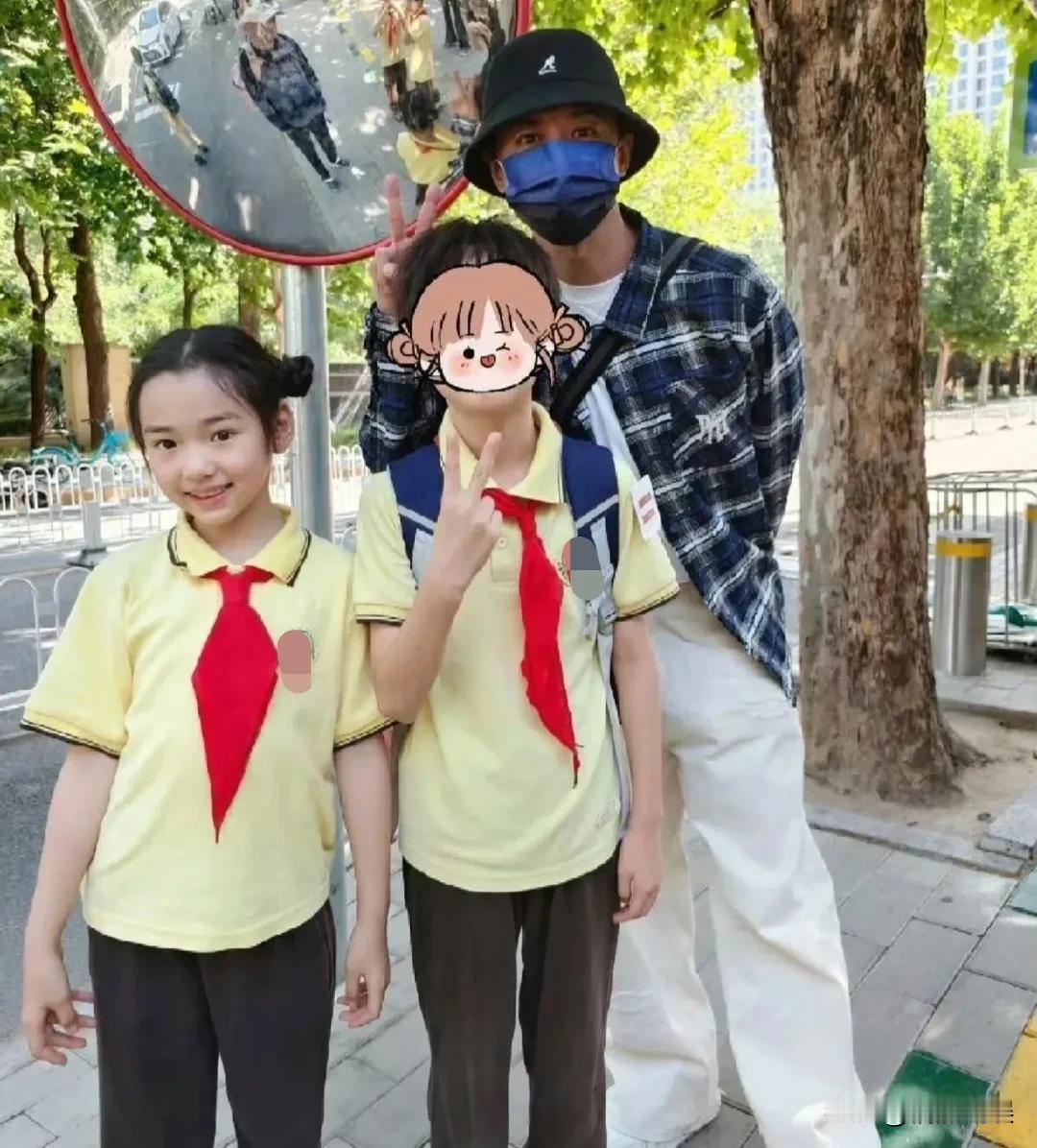 张维伊在北京，接继女小酒窝放学。他戴着渔夫帽和口罩，穿着格子衬衫白色裤子，这穿
