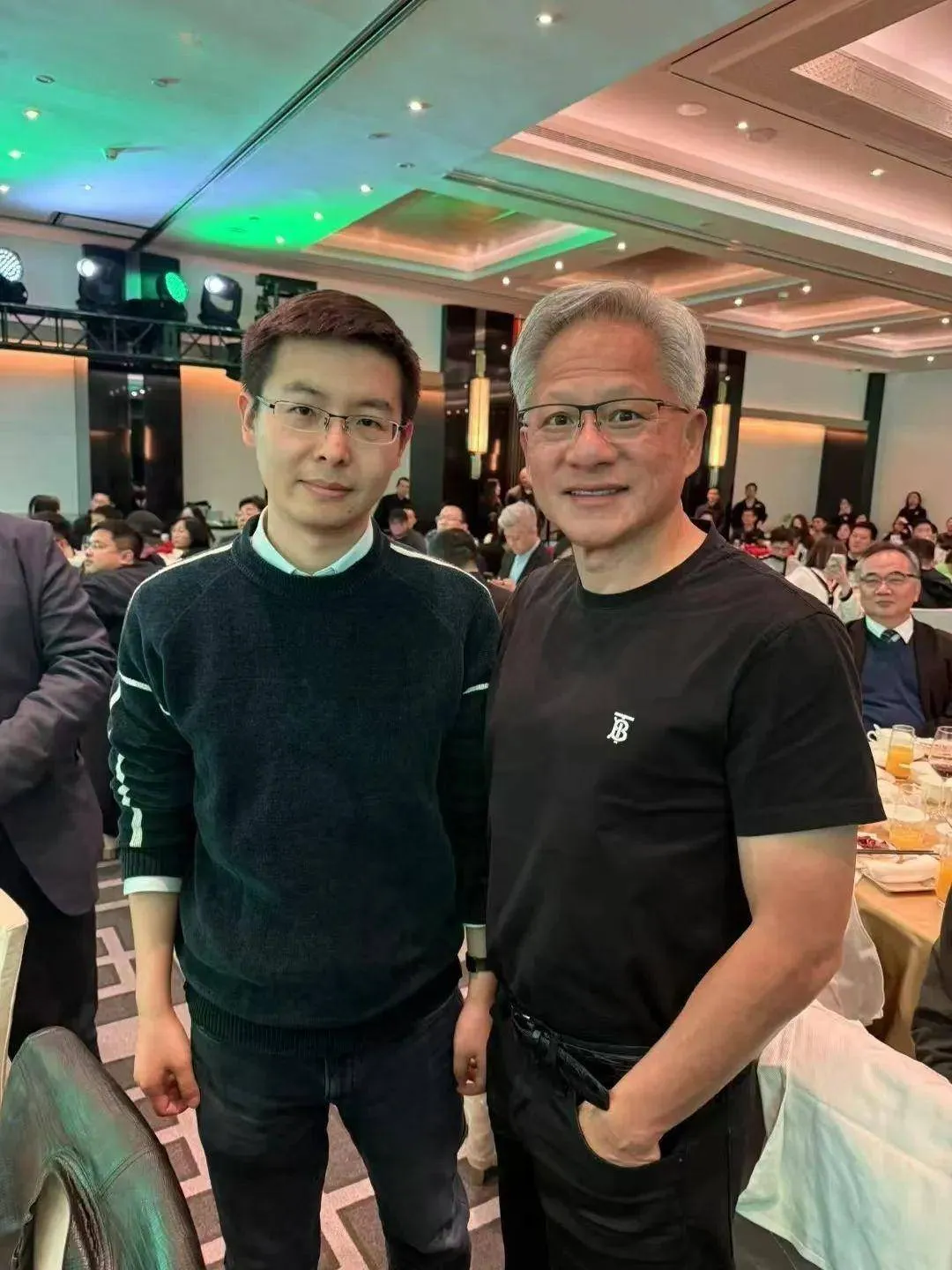 千亿富豪黄仁勋和宇树科技创始人王兴兴一起合照，黄仁勋手插裤兜，非常有富豪的气质，两个有钱人都戴了眼镜