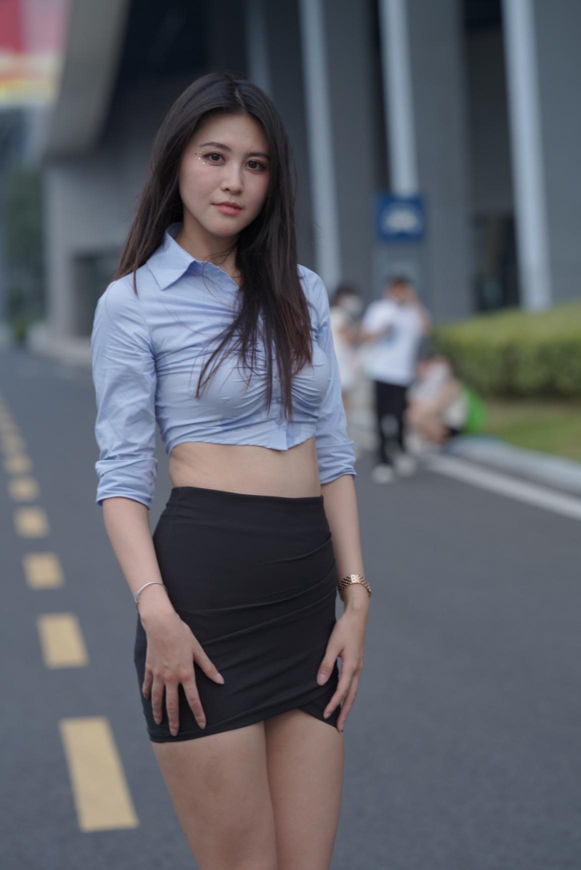 浅蓝短款衬衫揉着通勤的利落，收腰设计露了点柔，袖口挽起的弧度裹着随性；黑裙的褶皱