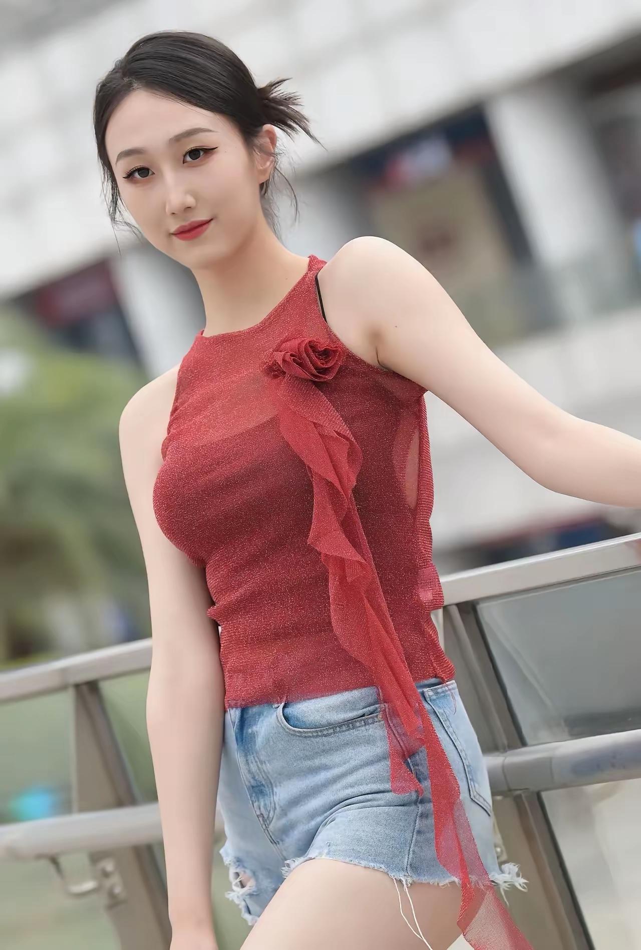 这姑娘穿着红色上衣和牛仔短裤，站在户外。