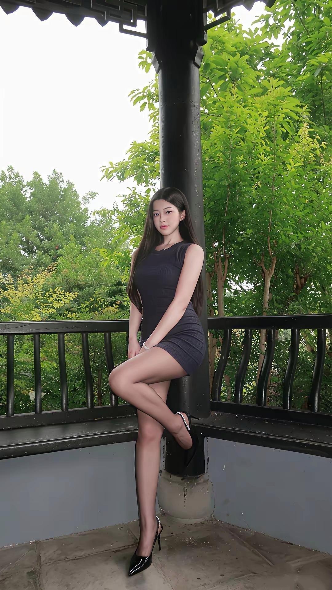 身着深灰色无袖包臀短裙，搭配黑丝与尖头细跟高跟鞋，精致修身，凸显出流畅的身材线条