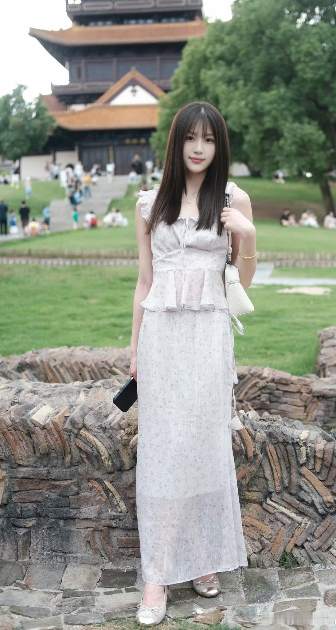 美女身穿轻盈白裙，优雅漫步在古风建筑前，感受历史与现代的交融。