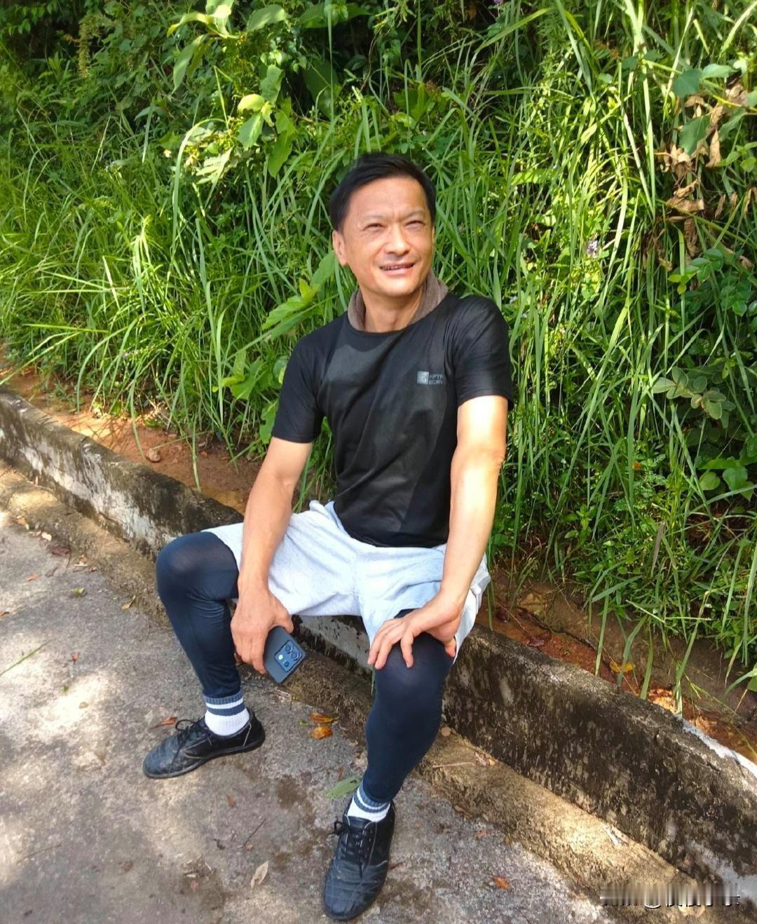 59岁TVB男星陈锦鸿在香港爬山，累了坐在路边休息。他穿着一身朴素的运动服，脸部