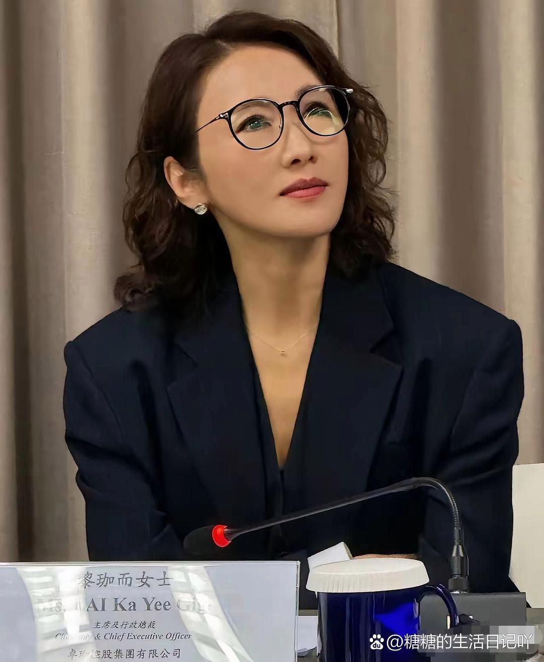 54岁的黎姿以集团主席兼总裁的身份出席股东大会！她穿着黑色西装带着黑框眼镜，显得