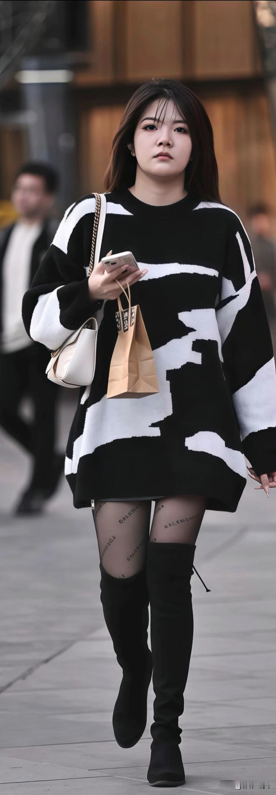 街头看到位女生，黑白花纹长毛衣配黑过膝靴，简单又好看。手里拿着手机和小袋子，这样