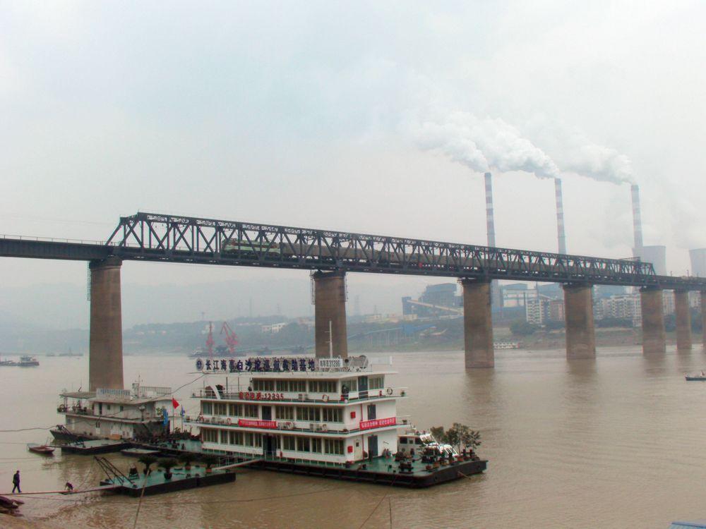 2010年的川黔铁路白沙沱长江大桥，一列货运列车正通过该桥，桥对岸的烟囱就是珞璜