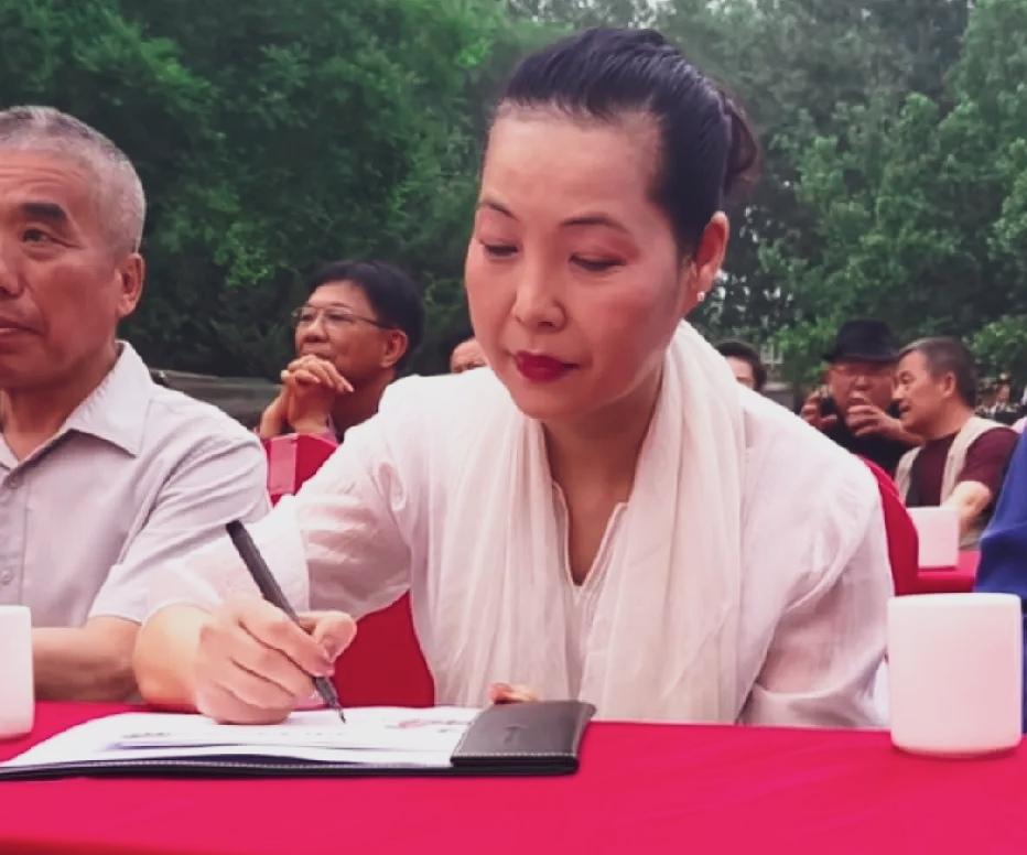 梦鸽老师为现场粉丝签字的现场，素雅的白衣，搭配同色系披肩，利落的盘发，特别有风韵