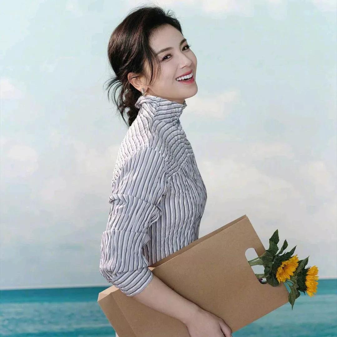 阳光沙滩上的快乐女孩，手捧鲜花，心旷神怡。海边花海少女海边度假少女海边微笑美