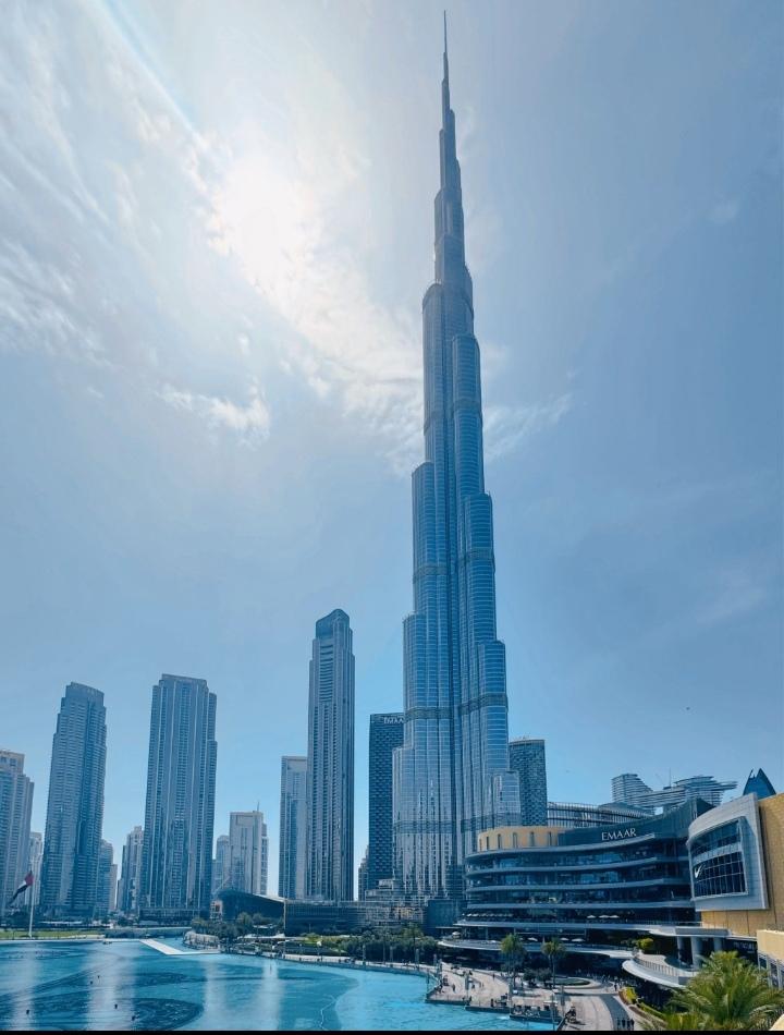 晴空下，迪拜哈利法塔刺破云层，玻璃幕墙折射着日光，与周边摩天楼并肩成城市天际线。