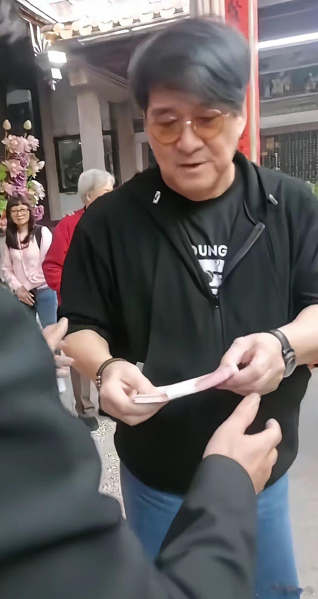 周华健满脸堆笑拿出一W块钱并交代着什么给周氏祠堂主事人，周围人露出难以置信表情，