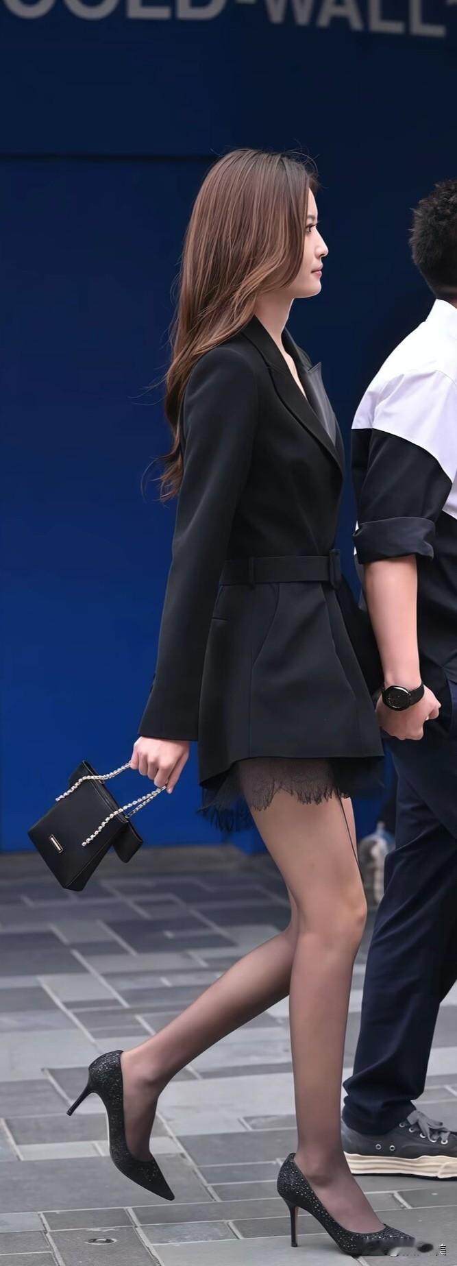 一身黑色收腰西装裙，腰带勾勒腰线，暗藏蕾丝细节增添精致感。搭配黑丝与闪钻尖头高跟