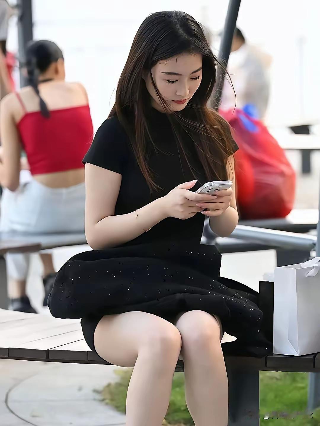 一个穿黑裙的女孩在长椅上玩手机。黑裙感美女