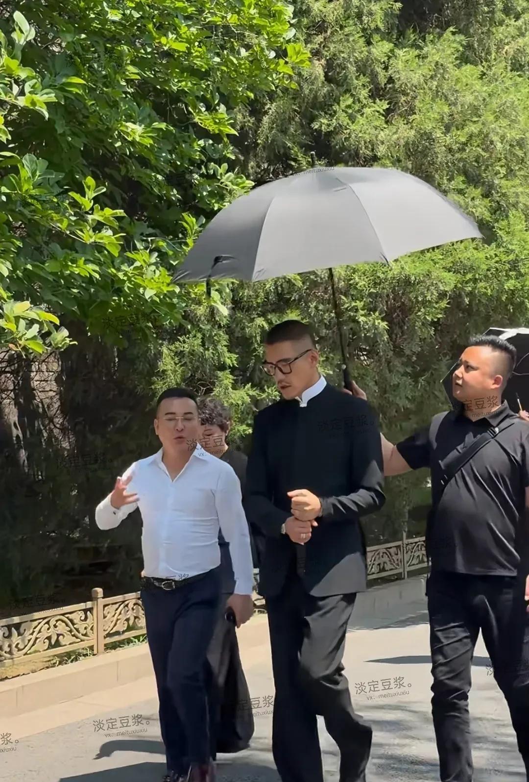 看模特胡兵的派头，边上穿白色衬衫的像在给他介绍着什么，一位在给他打着伞，两位都比