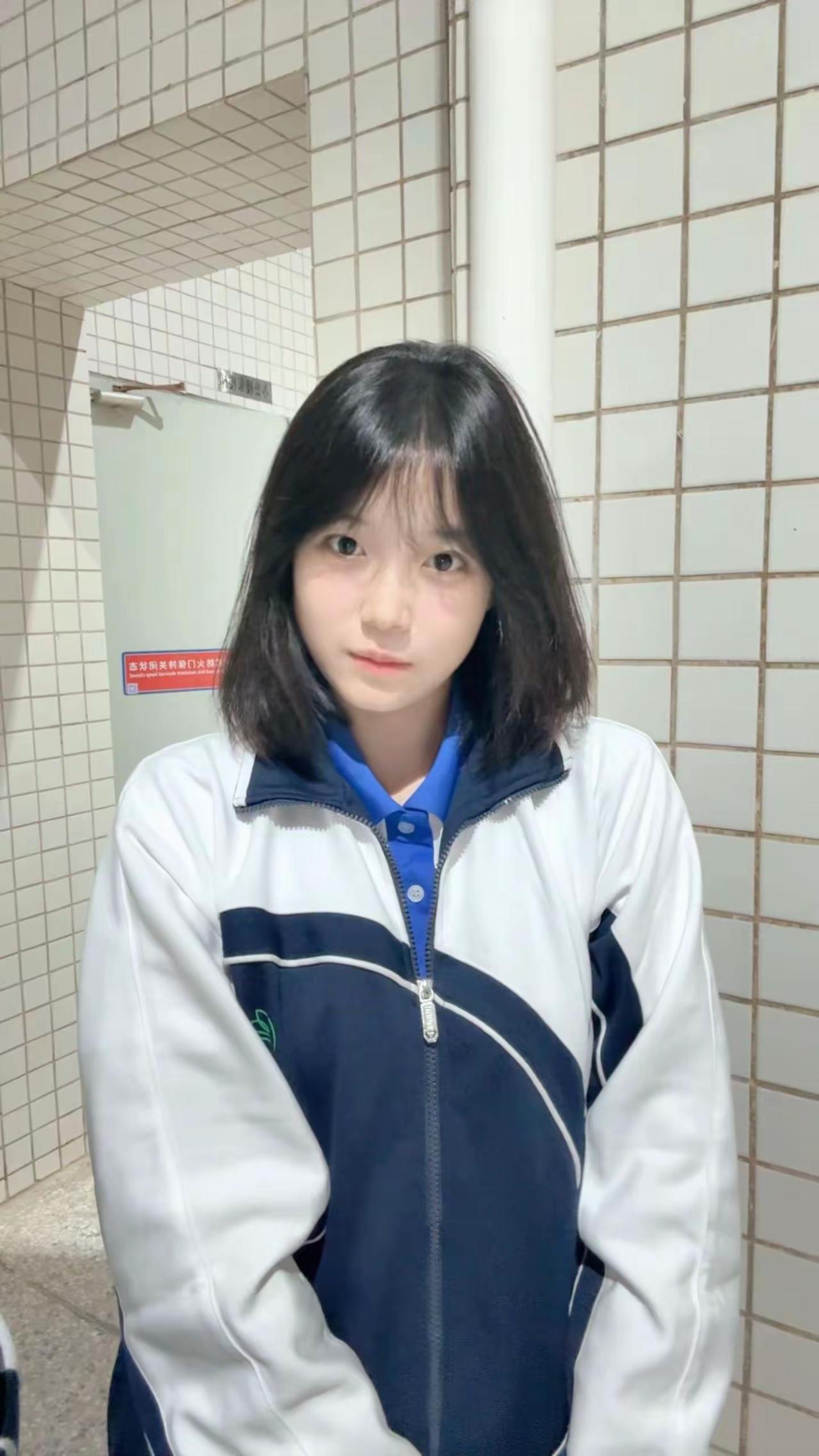 这女生穿着校服，站在洗手间门口。