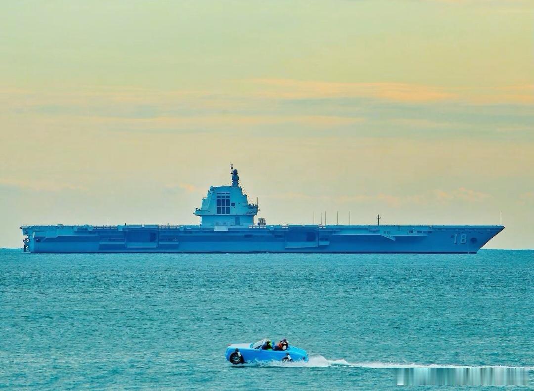 福建舰再次出海训练，缓缓驶出三亚军港，照片前景是在三亚海滨景区游玩的快艇，这一次
