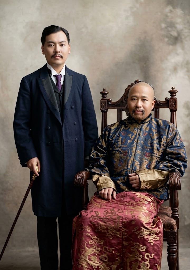 照片中，右侧坐于雕花椅、着长袍马褂的老者为康有为；左侧站立、着西式双排扣大衣、持