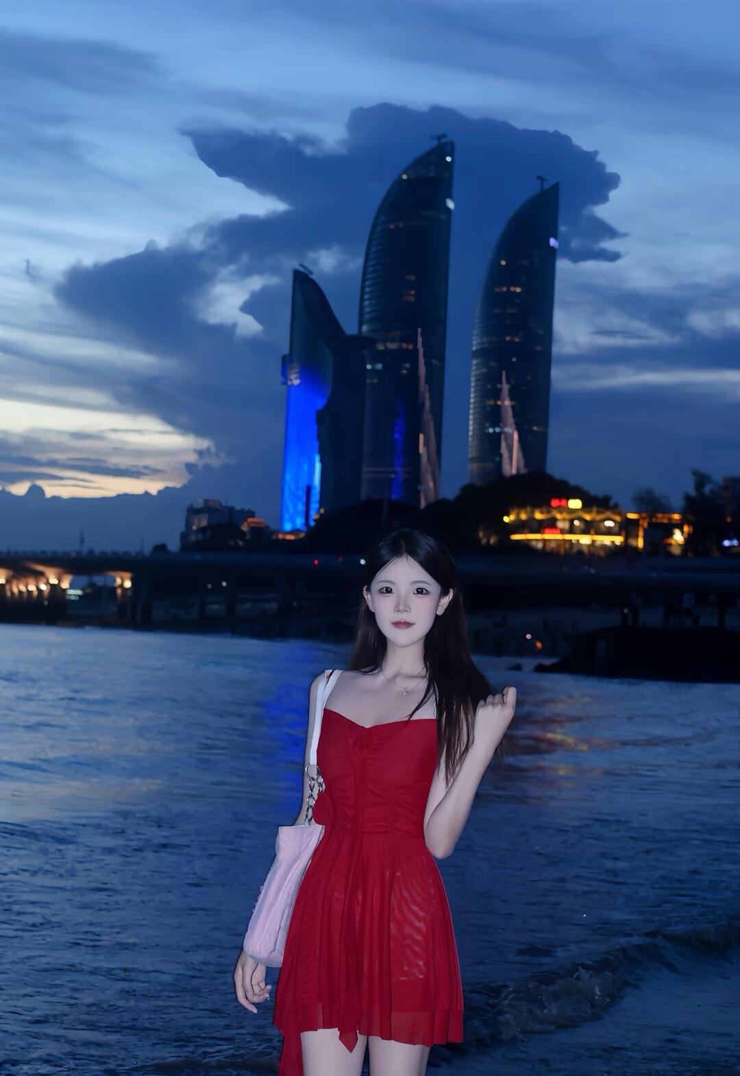 夜幕下的海边，红裙少女与现代建筑交相辉映，浪漫迷人。