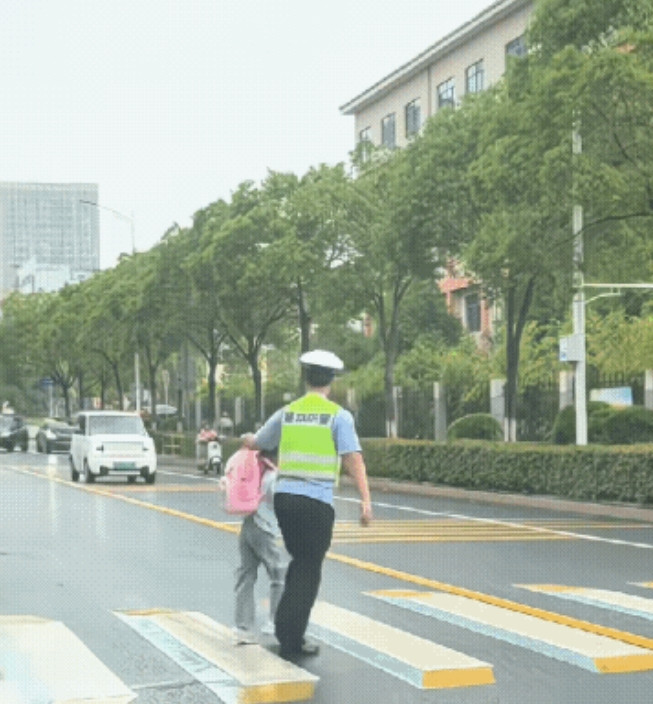 学校门口暖心一幕，小女孩准备过马路，交警叔叔看到后，示意她过去并帮忙拧起书包护送