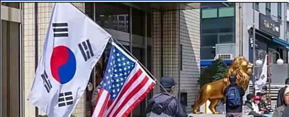 韩国民众举着美国国旗搞反华游行，其中有个游行者正好碰到一位去韩国旅游的中国游客，