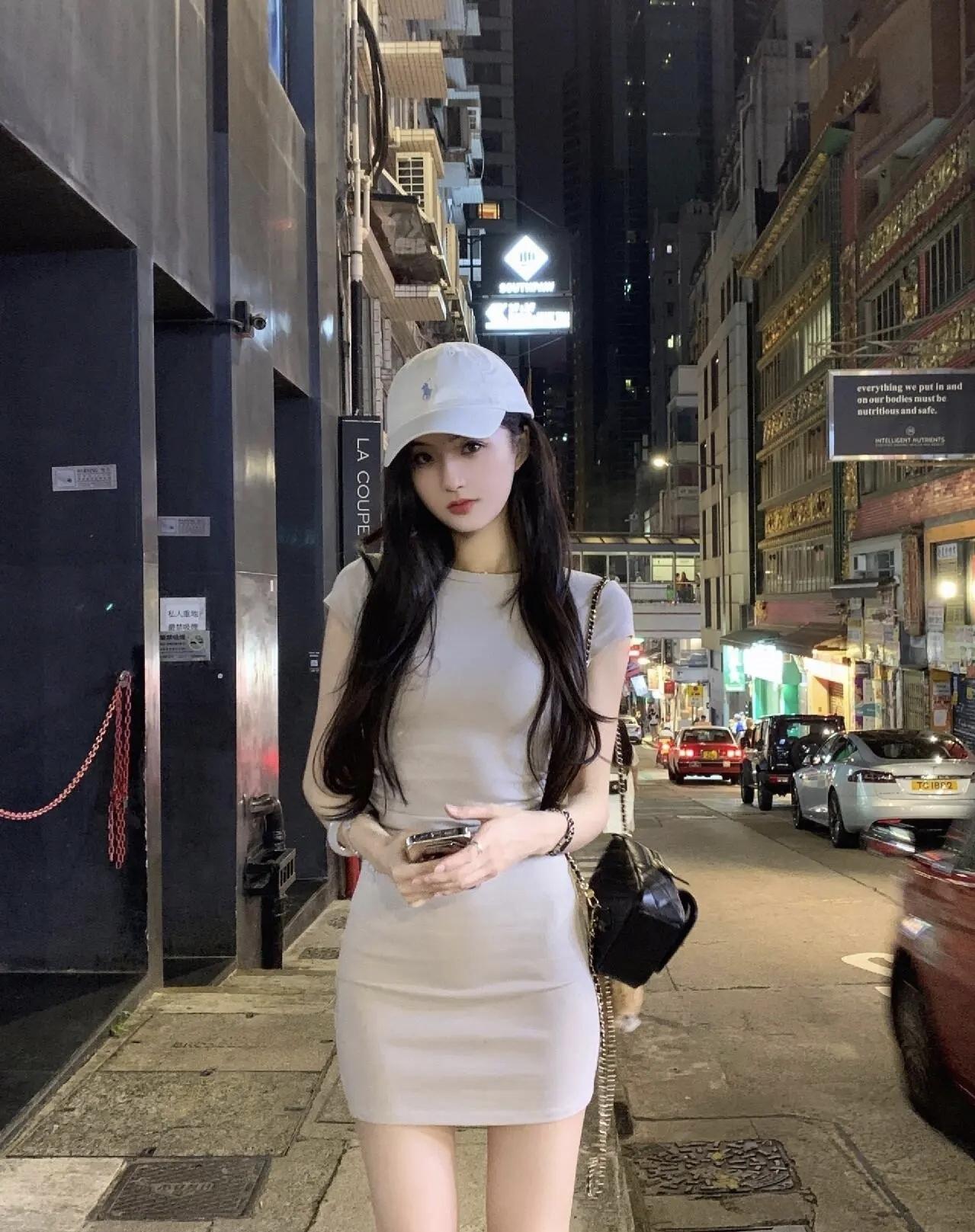 香港街头的晚风里，浅灰裙装配棒球帽，在霓虹与烟火气中，邂逅松弛又时髦的夜。