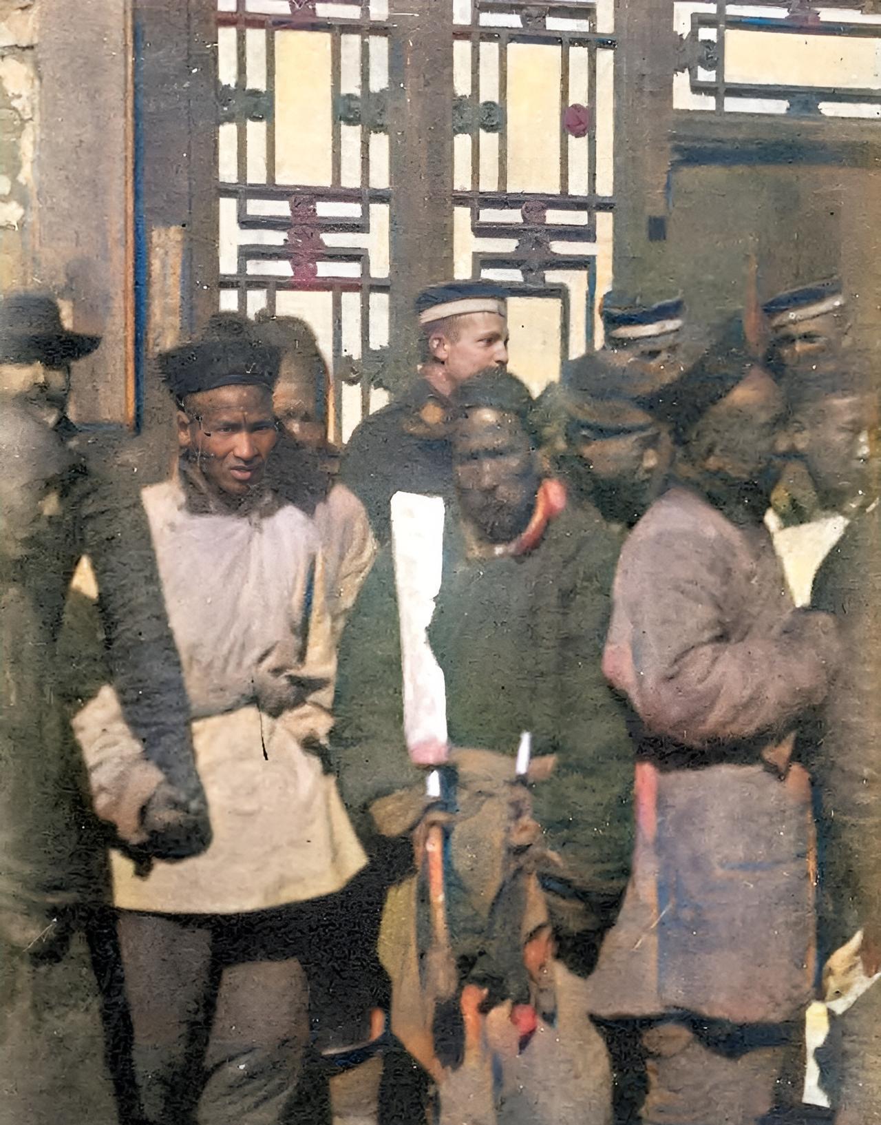 1900年12月31日，两名正要行刑的刽子手抱着大刀站在人群前。这把行刑的大刀与