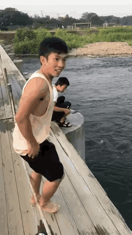 一位年轻男子，在桥上脱掉上衣外裤展现出健硕的身材，对镜头笑了笑，一跃而下跳进了河