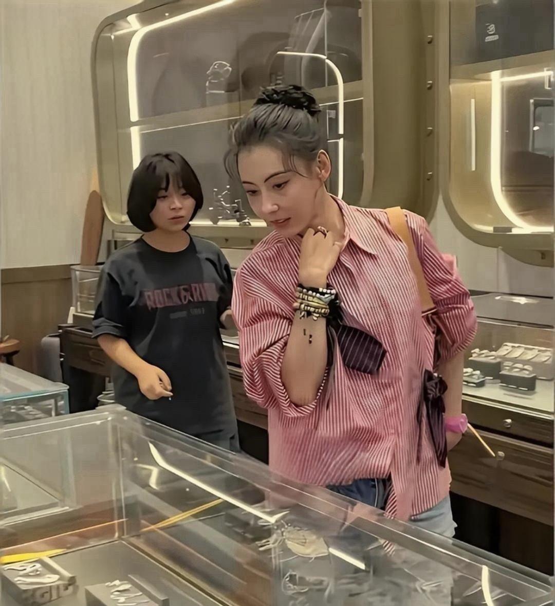 46岁张柏芝现身三亚周大福门店，穿粉色条纹衬衫搭破洞牛仔裤。她头发盘得很利落，皮