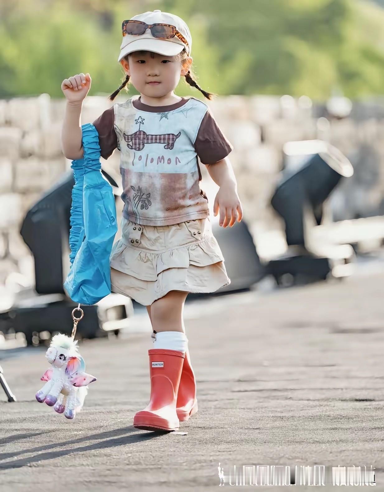 闪闪发光时装周上，两岁的闪闪手提挎兜，穿着一双橘色筒靴，迷你蛋糕裙，卡通T恤，