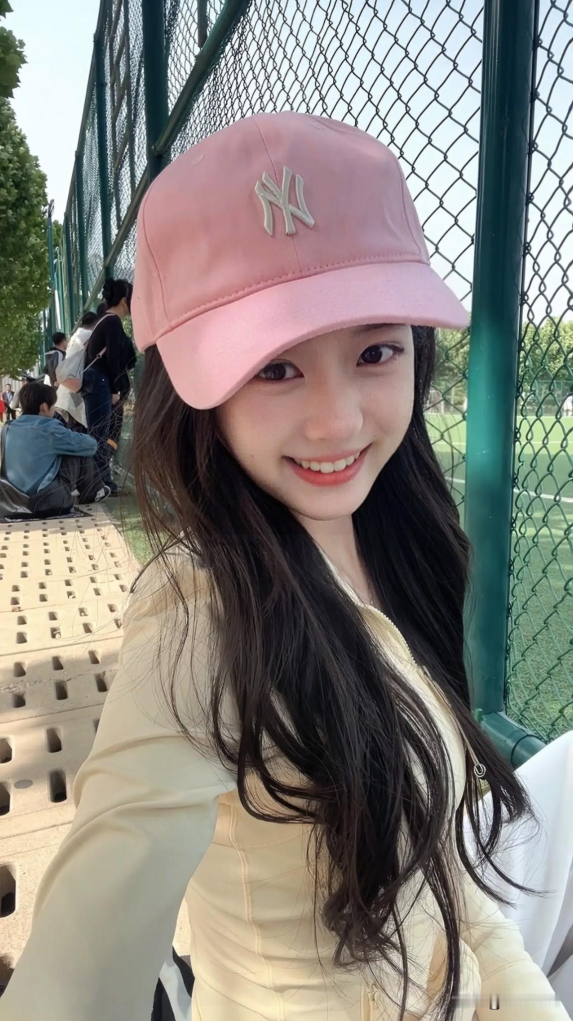 阳光明媚的午后，少女戴着粉色棒球帽，微笑面对镜头，散发着青春的活力与甜美。今日分