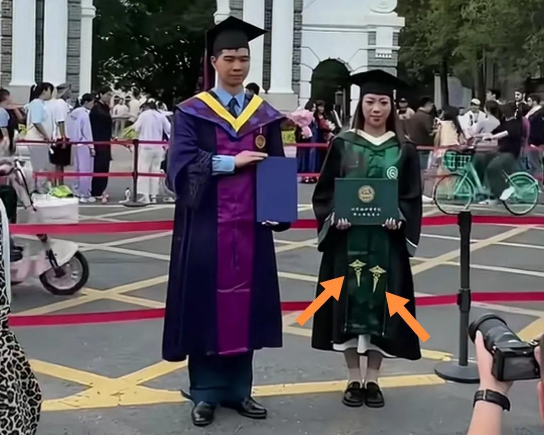 清华大学门前一女生穿绿色“双蛇杖”学士毕业服与男生合影。