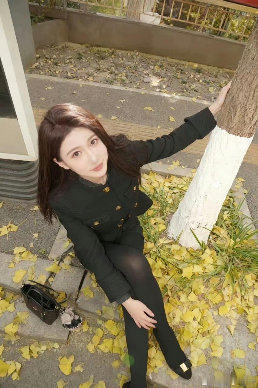 秋日暖阳下，黑衣少女倚树而坐，落叶飘零，静谧美好。