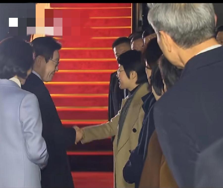 李在明上海机场返程，3个细节:1、登舷梯前一位女士送了一本访华画册，应该中方人