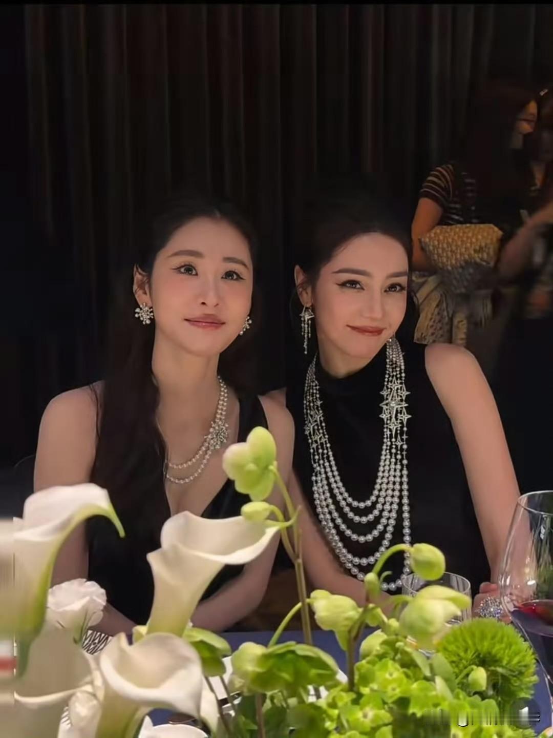 这场晚宴同框照反差感十足，迪丽热巴身着黑色无袖礼裙，叠戴满钻珍珠项链，浓颜妆容明
