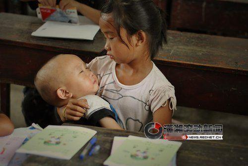 2011年，支教志愿者卢七星，在教室拍下一张照片，一个7岁小女孩，抱着一个1岁的