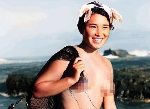 1955年，一名身体强壮的日本女人赤裸上半身，背着一个黑色的编织袋站在海边。这个