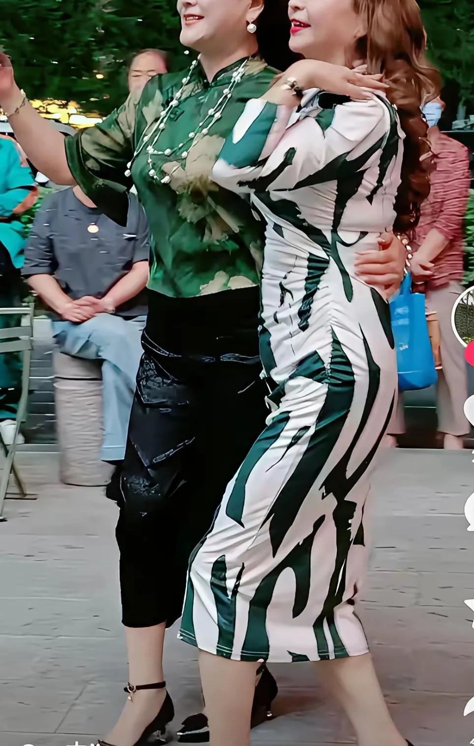 两位女士在公园里跳舞，她们的裙摆随风摆动，笑容灿烂。公园里的大妈广场舞也是人才济