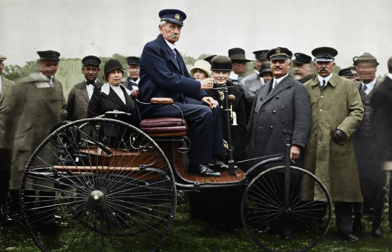 这是一张承载着汽车工业起源记忆的历史照片，画面核心是卡尔·本茨，他身着深色西装，