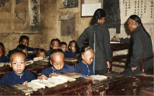 这张老照片拍摄于清末民初，一所新式小学堂教室。照片中，教室昏暗简陋、墙壁斑驳，学