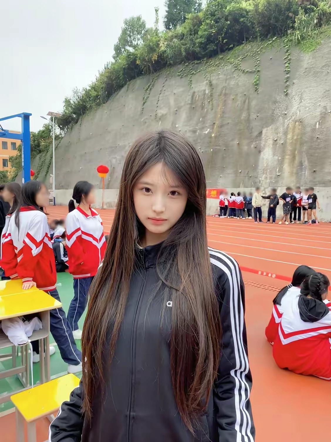 操场上的姑娘穿着黑色运动服，背景有同学们在活动。